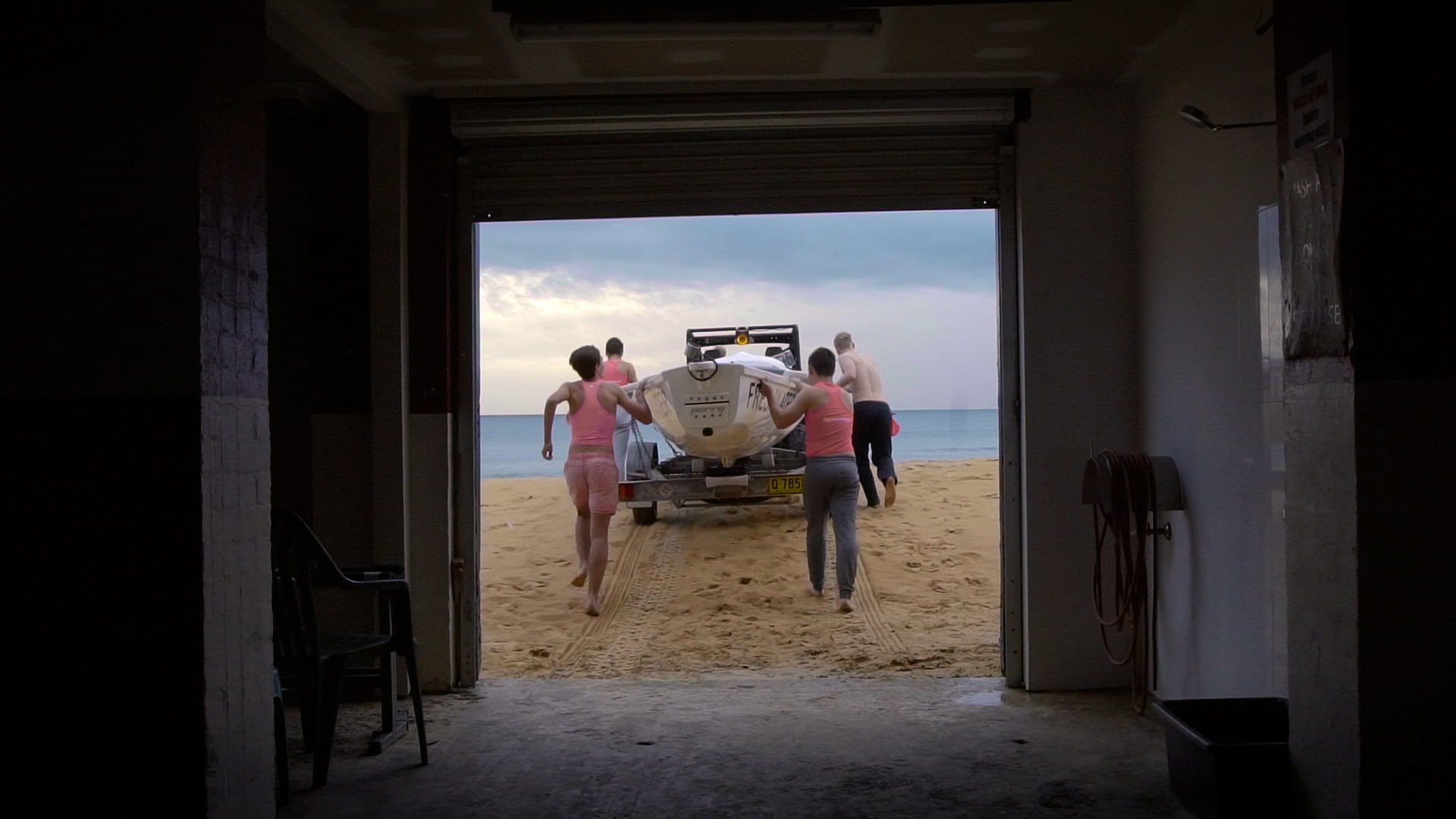 Four men pushing a row boat out from a garage onto the beach.