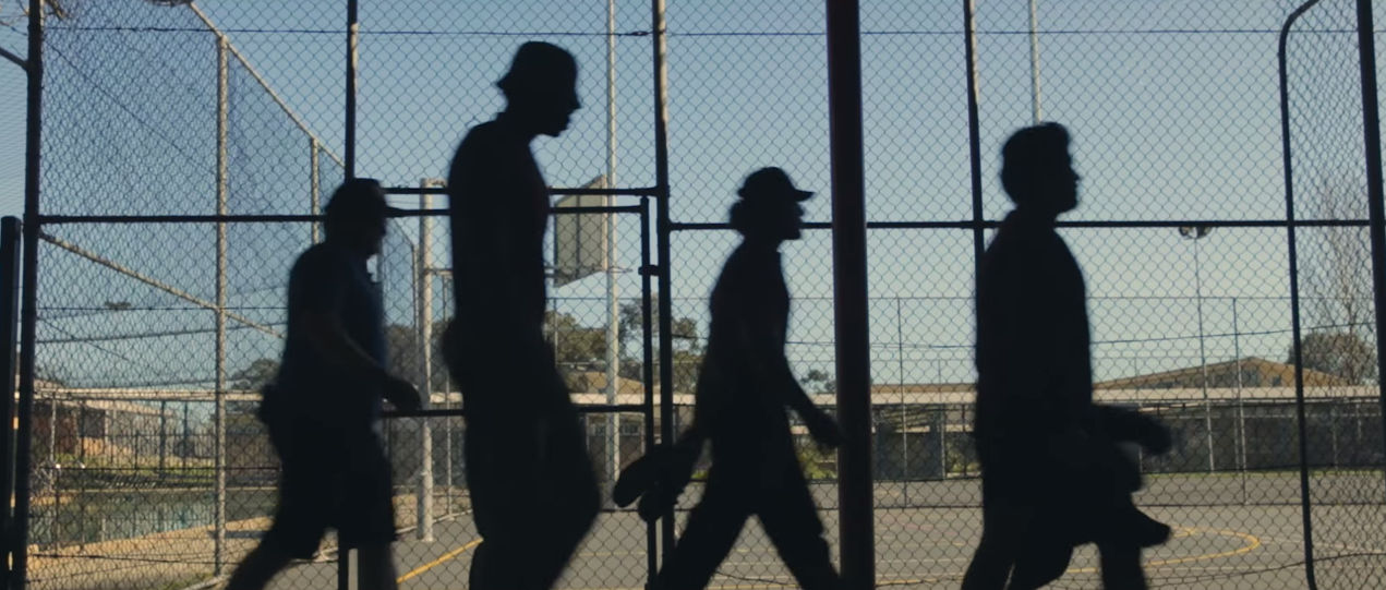 Four silhouettes of boys walking past basketball court.