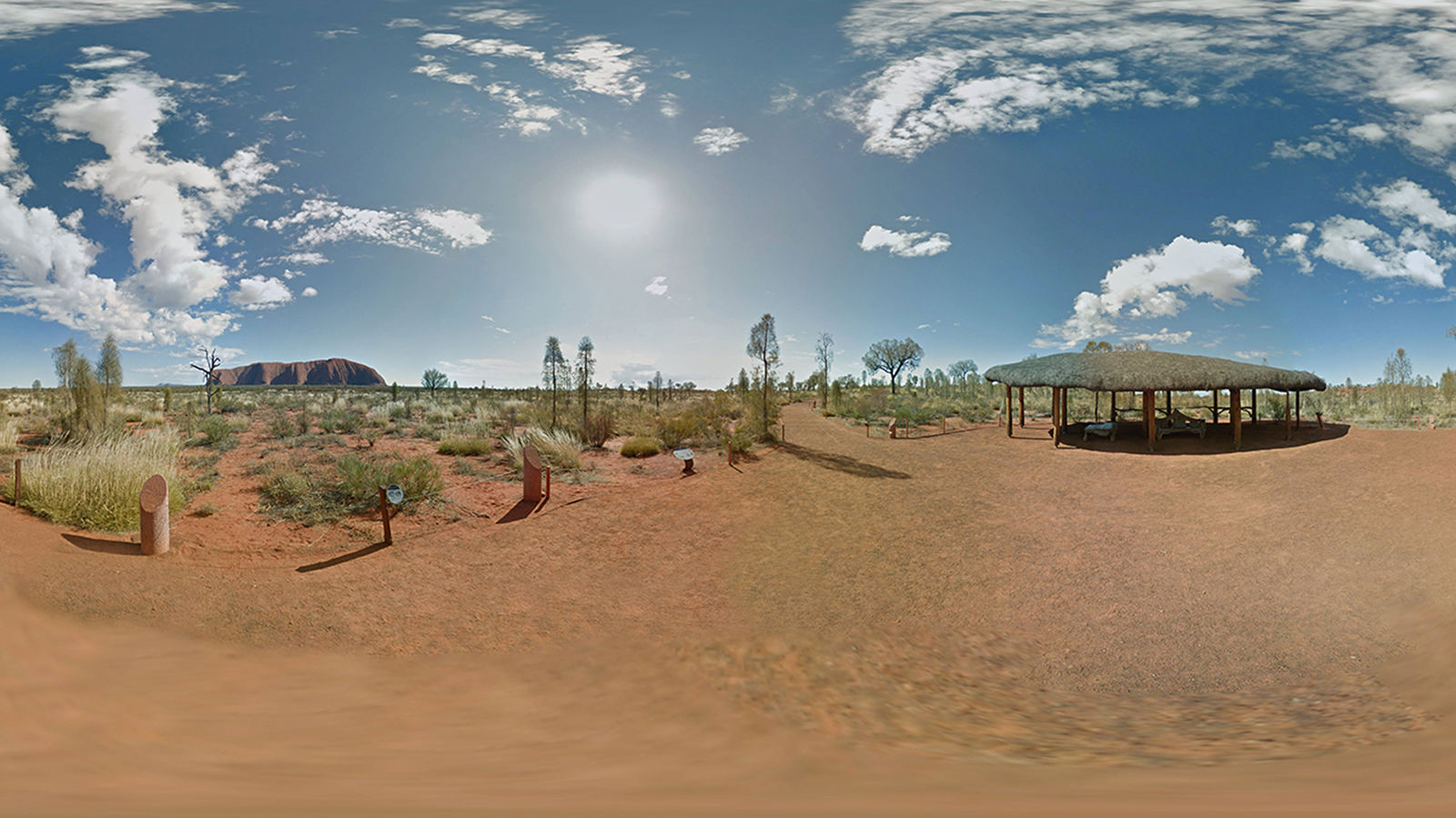 Wide-shot of the Australian desert with Uluru in the background.